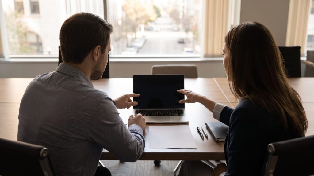 Two colleagues reviewing a credentials checklist for a robotic surgeon bio page at a conference table
